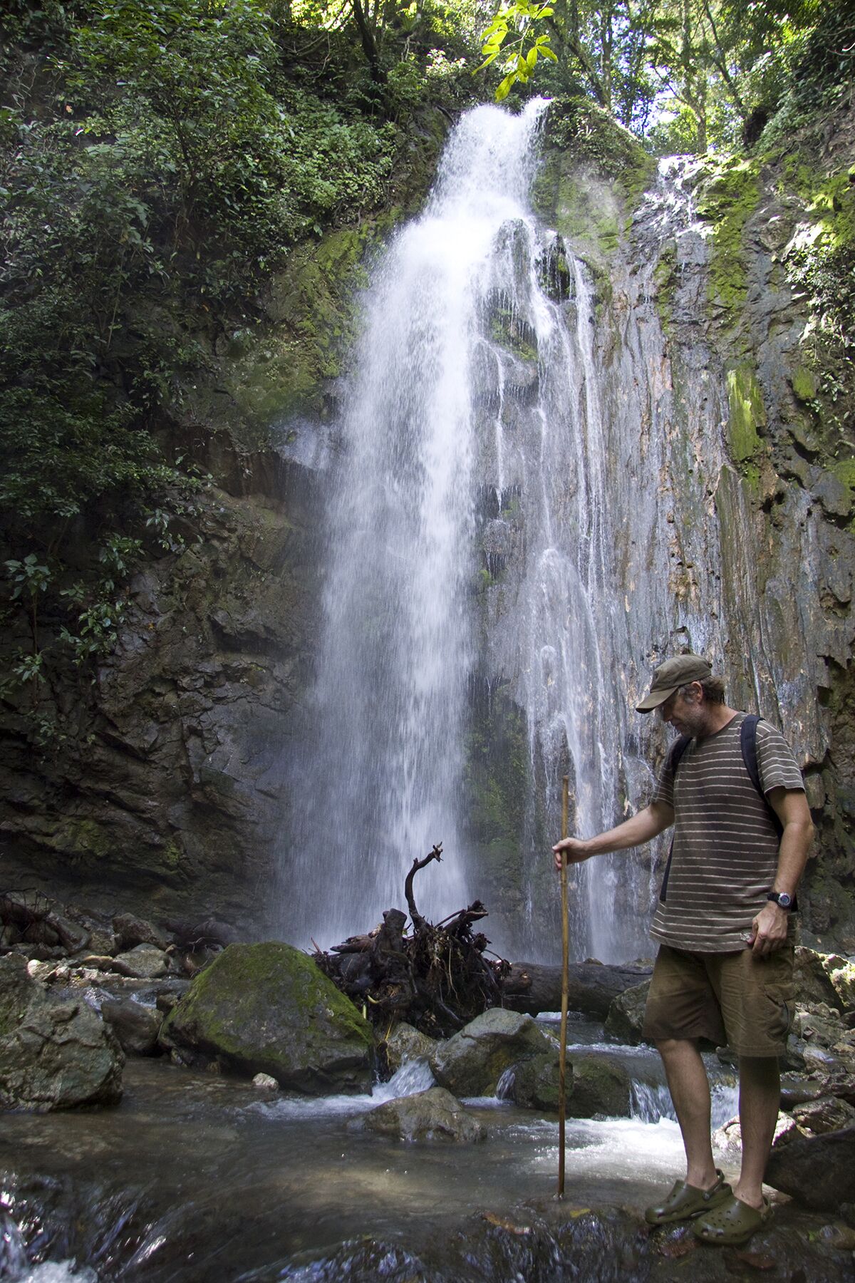 A waterfall in a forested area with a person standing near the water's edge.