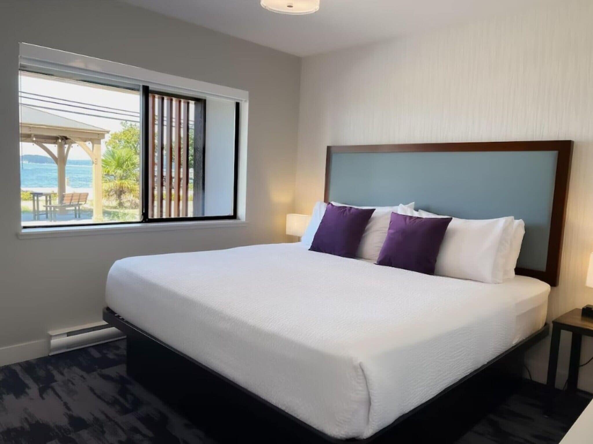 Habitación de hotel con una cama grande, una ventana con vista al mar y una mesita de noche con una lámpara.