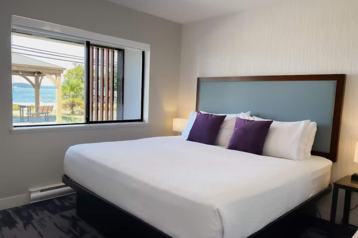 A hotel room with a large bed, a window with a view of the sea, and a nightstand with a lamp.