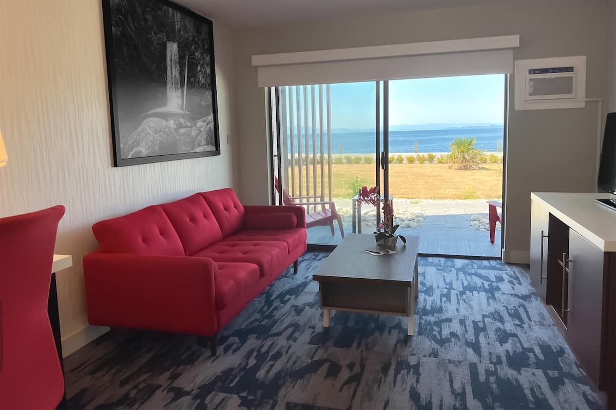 A modern living room with a red sofa, a coffee table, and a view of the sea through large sliding doors.