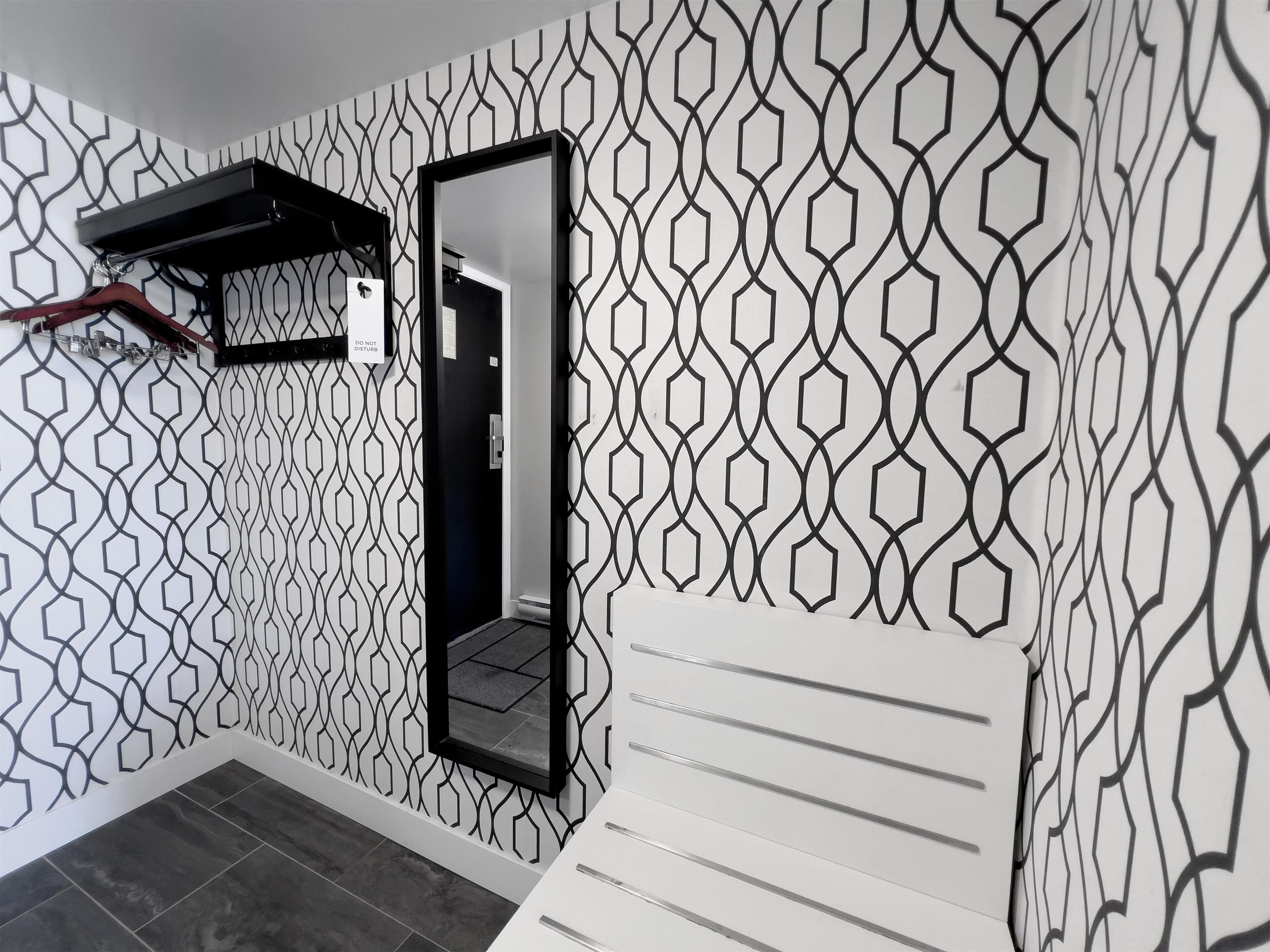 A room with a geometric patterned wall, a black-framed mirror, a white cabinet, and a black hanging rack.