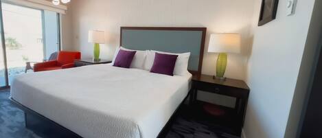 A hotel room with a large bed, two nightstands with lamps, a red chair, and a view through the window.