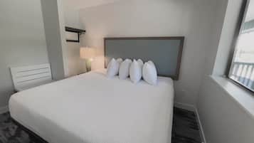 Habitación de hotel con una cama grande, una mesita de noche con lámpara, una ventana con vistas y un cabecero con varios almohadones.