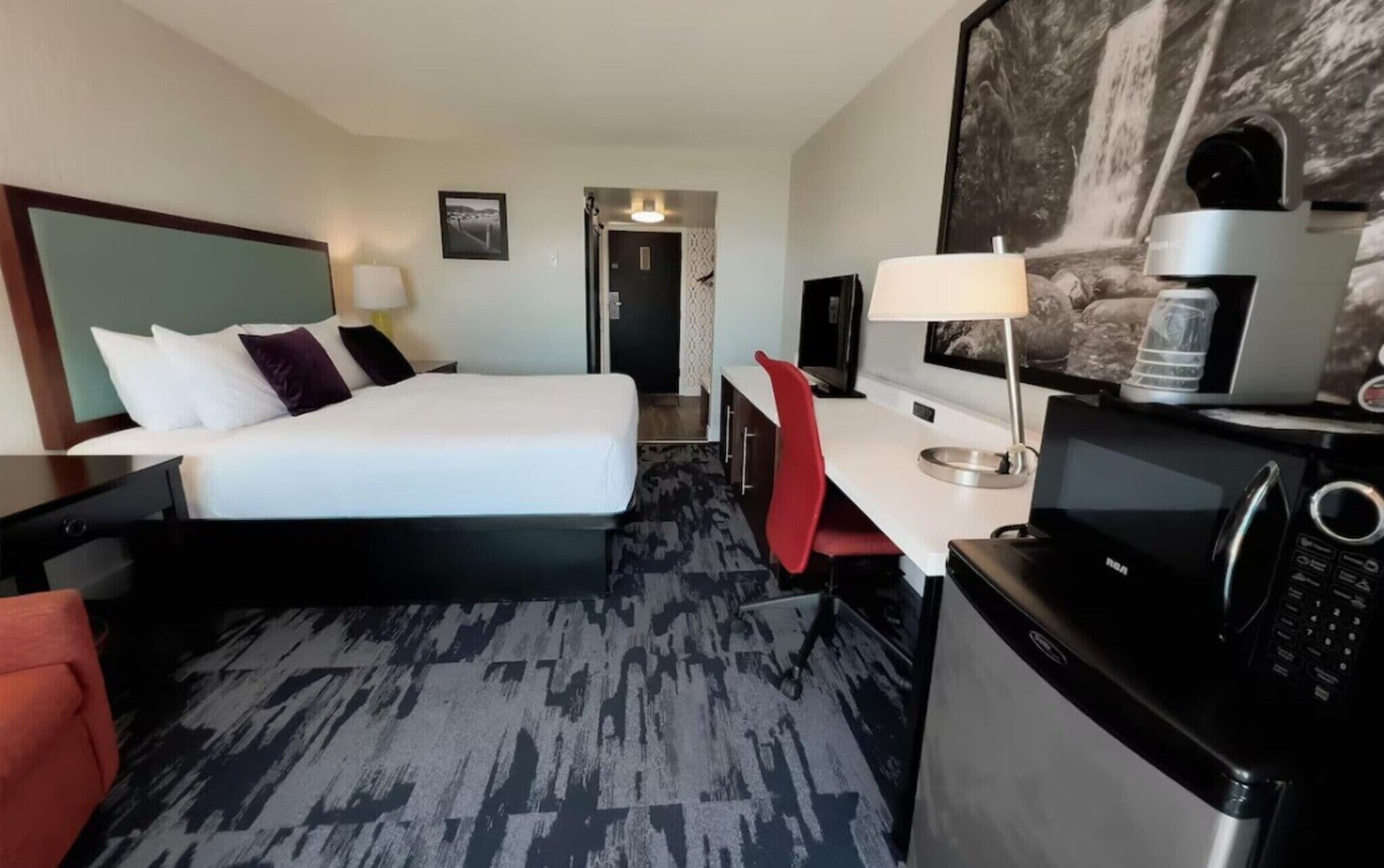 Una habitación de hotel con cama, escritorio, silla y microondas.