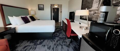 A hotel room with a bed, desk, chair, TV, microwave, and a water dispenser.
