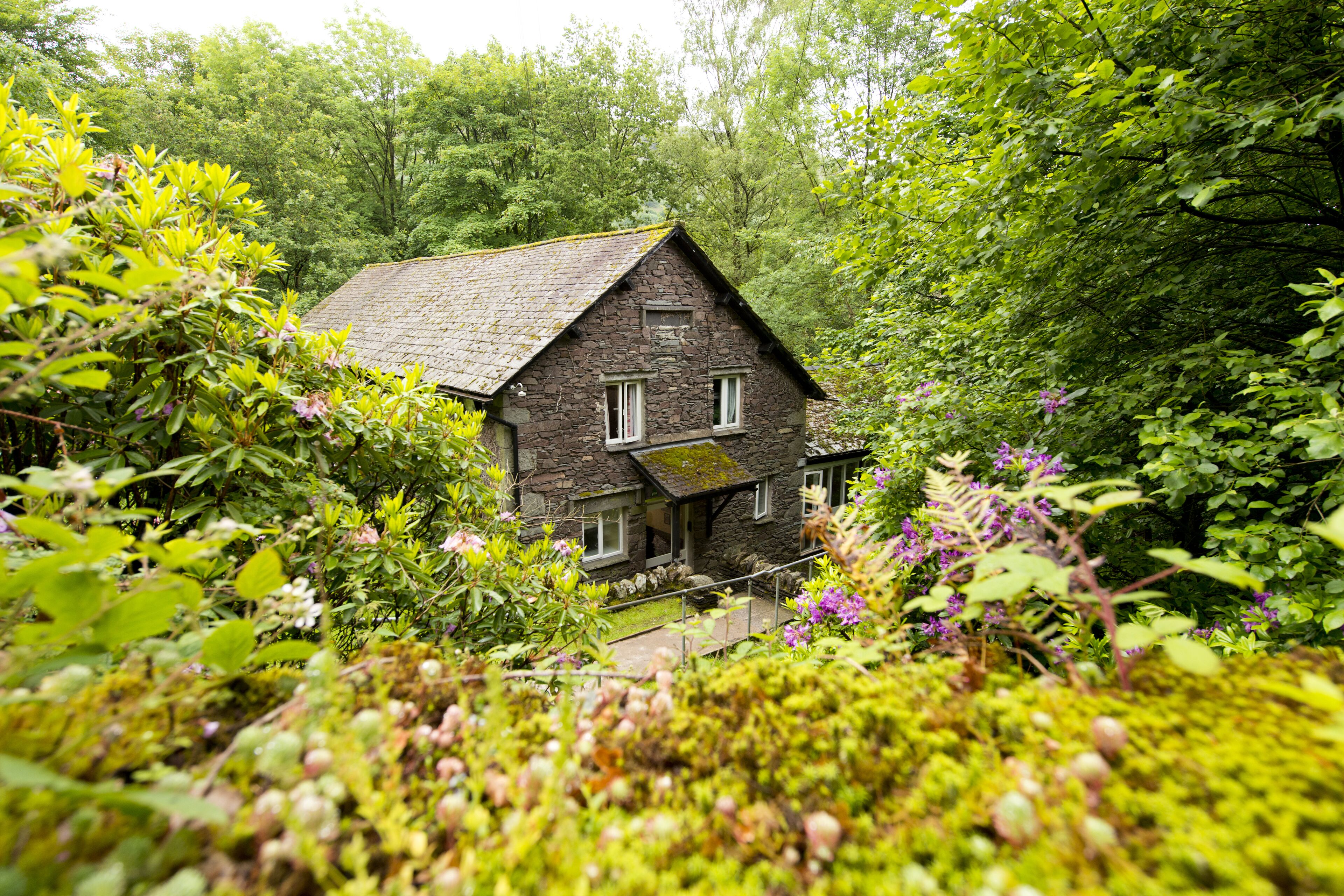 Una casa de piedra rodeada de abundante follaje y plantas en flor.