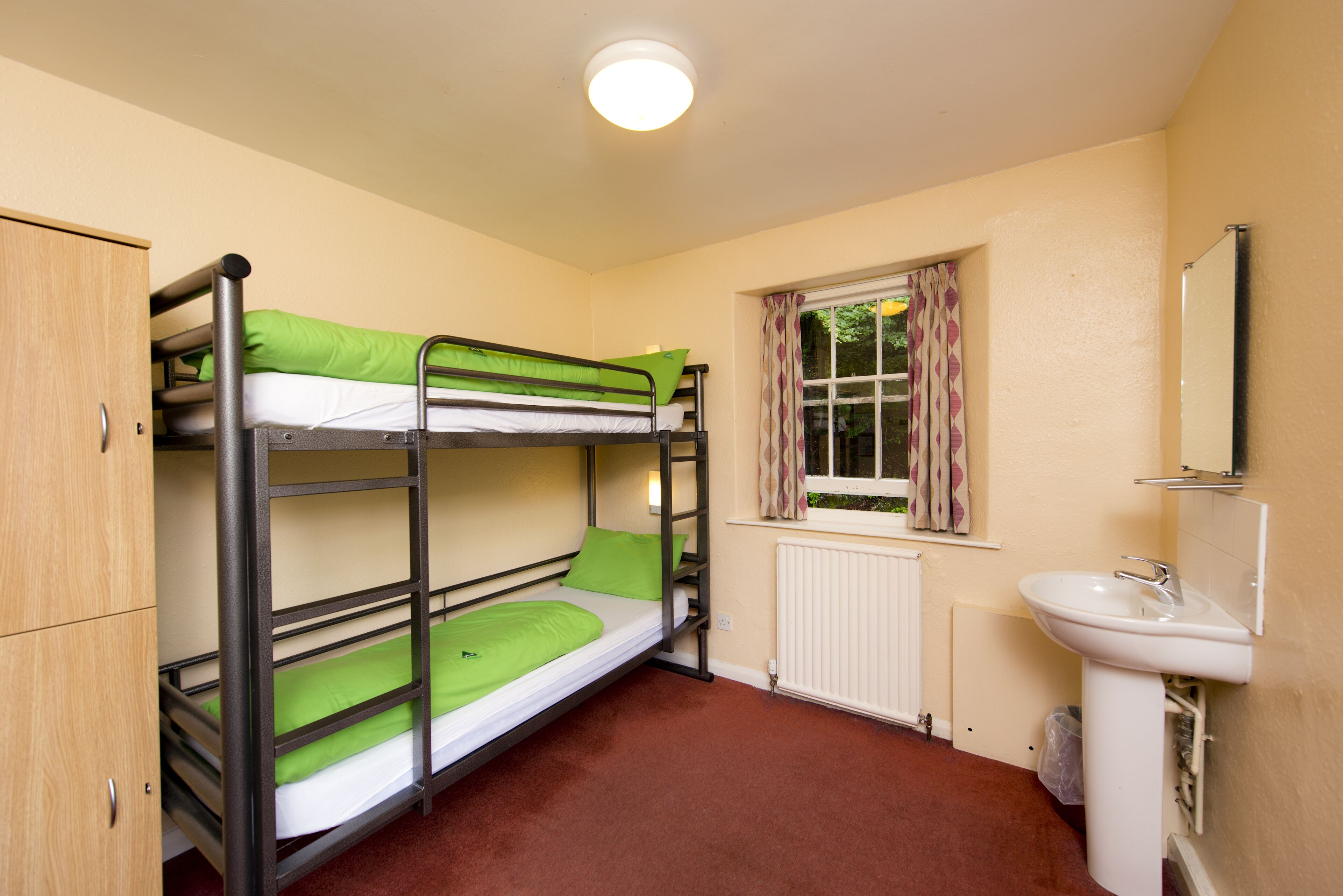 A bunk bed room with a window, radiator, sink, and wardrobe.