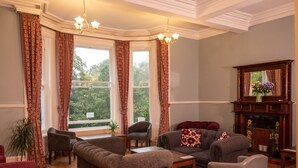 A cozy living room with a fireplace, comfortable seating, and large windows with curtains. - YHA Grasmere Butharlyp Howe - Hostel (Ambleside)