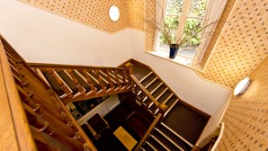 A wooden staircase with a view of a room below, a window with a plant, and patterned wallpaper. - YHA Grasmere Butharlyp Howe - Hostel (Ambleside)