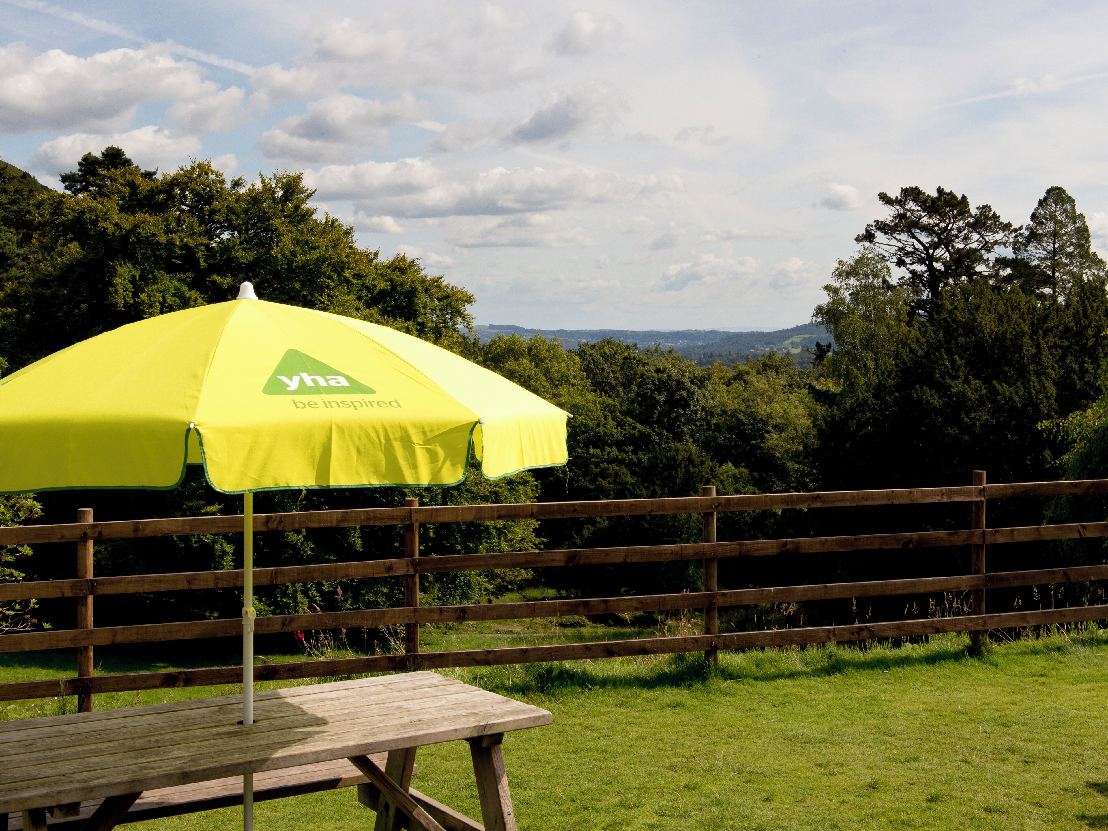 A wooden picnic table with a yellow umbrella branded with 'yha be inspired'.