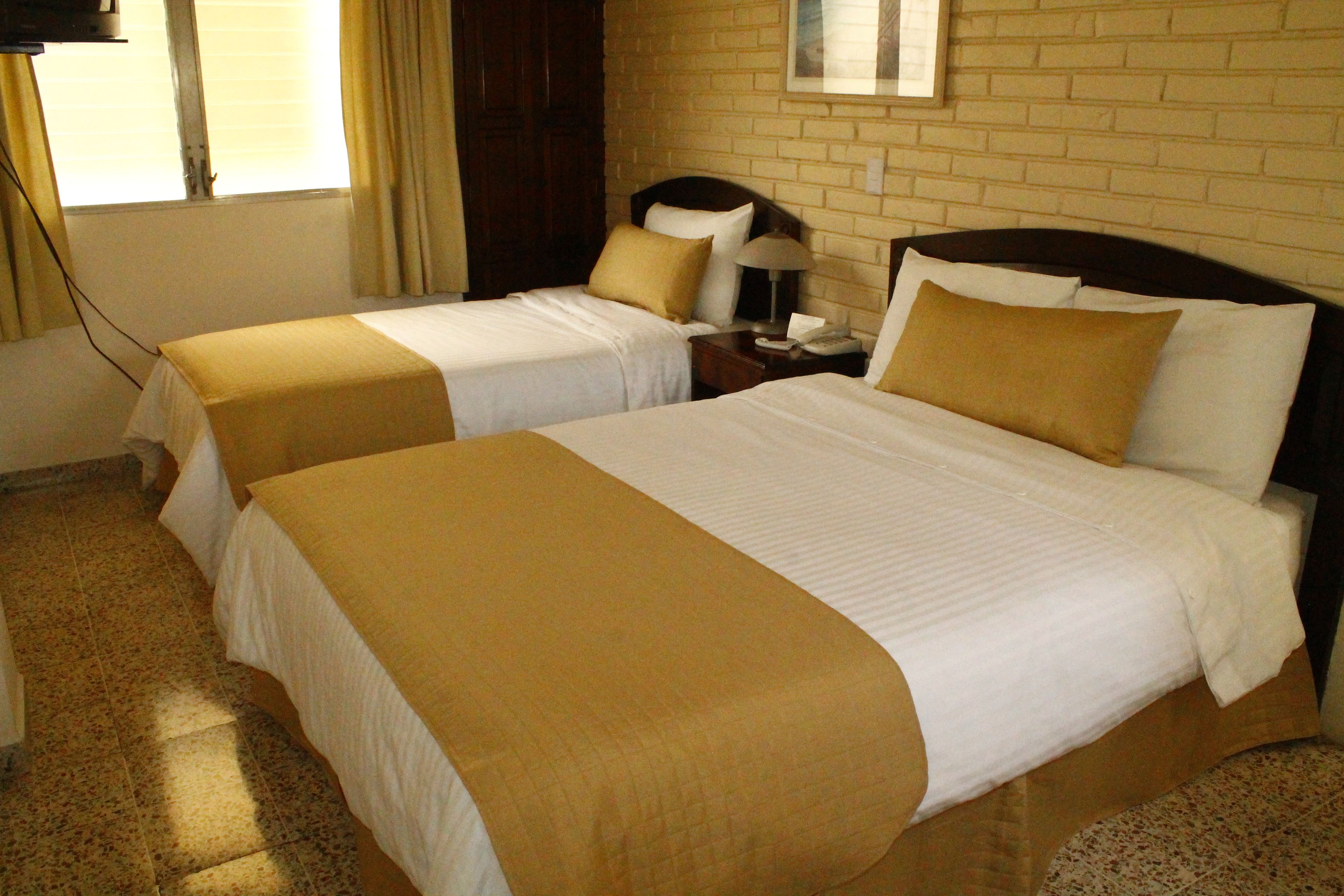 A hotel room with two beds, each with a white and beige bedspread, a wooden headboard, and a nightstand with a lamp.