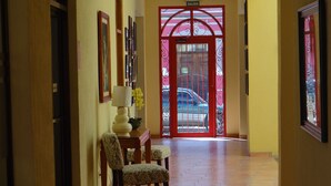 Un pasillo con una puerta roja, sillas con diseño, una mesa con lámpara y cuadros en las paredes.