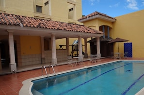 A swimming pool with a tiled deck, lounge chairs, and a covered seating area. - Hotel Mac Arthur (Tegucigalpa)