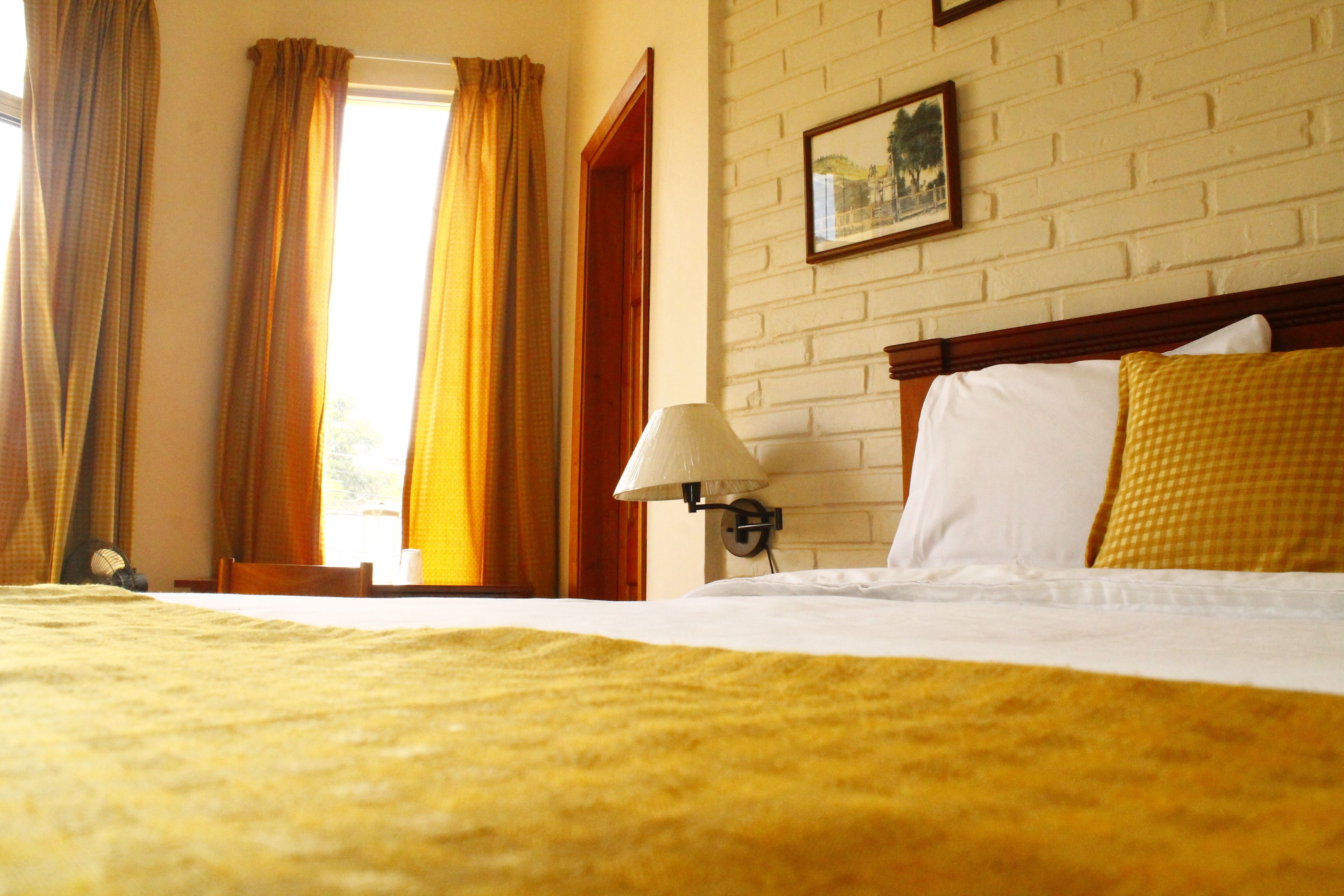 A hotel room with a bed, a lamp, and a window with curtains.