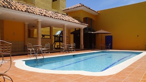 Una piscina con suelo de baldosas y sillas de metal alrededor.