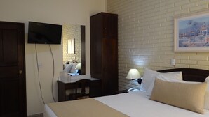 Una habitación de hotel con una cama, un escritorio, una silla, un televisor, un armario y un cuadro en la pared.