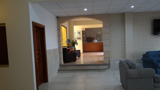 Un vestíbulo de hotel con una recepción, un sofá y un televisor montado en la pared.