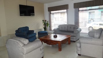 A living room with a grey sofa, blue armchairs, a wooden coffee table, and a TV mounted on a brick wall.