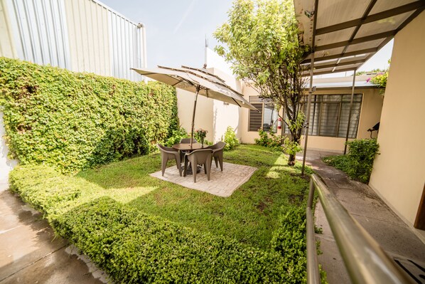 A patio area with a table and chairs under a canopy, surrounded by well-maintained hedges and a small tree. - Hotel Elizabeth Central (Aguascalientes)