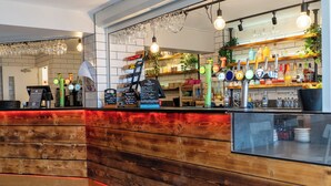 Una zona de bar con mostrador de madera, estantes con botellas y una pizarra de menú.