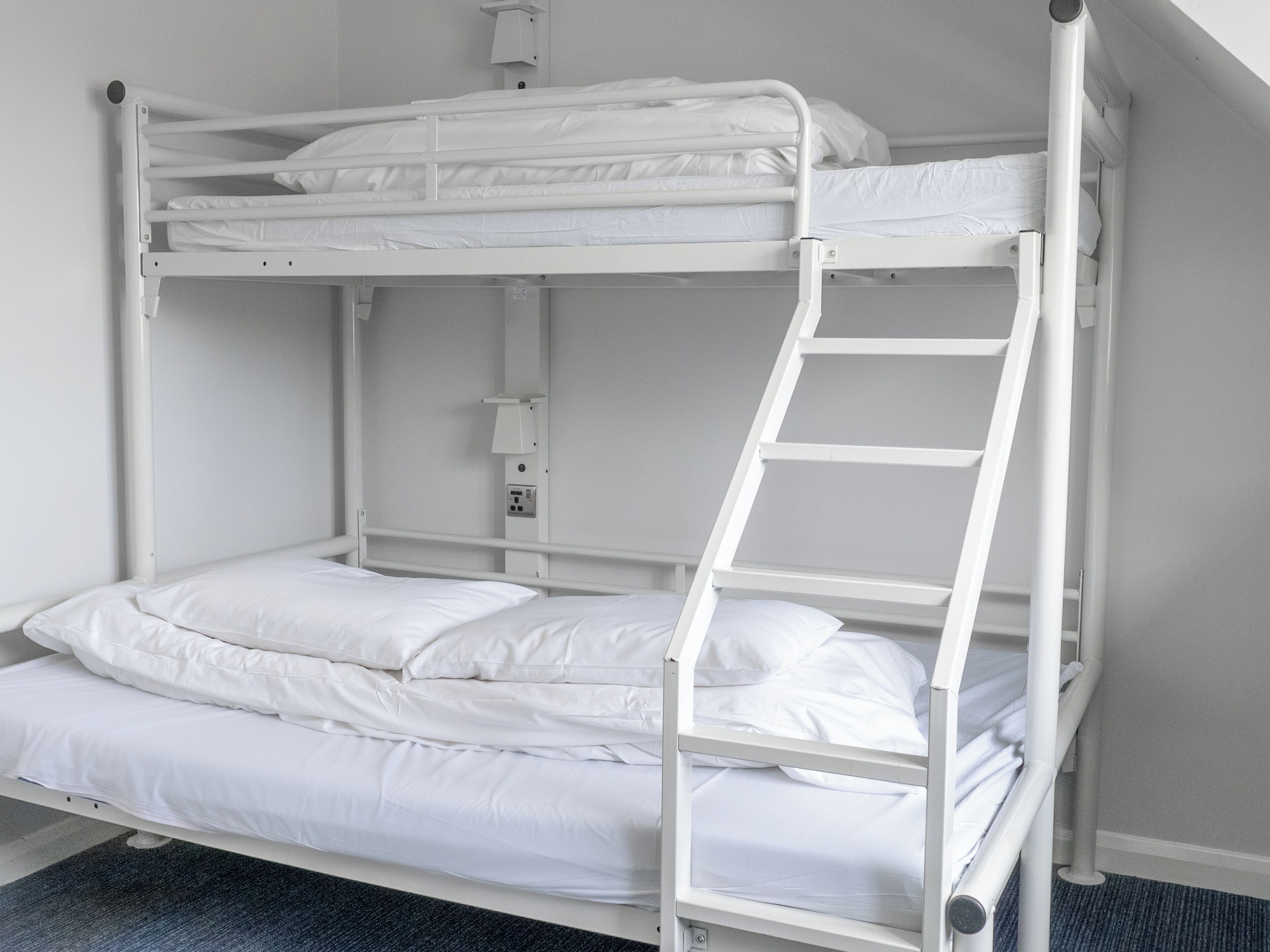 A bunk bed with a ladder, white bedding, and a small shelf with a light fixture.