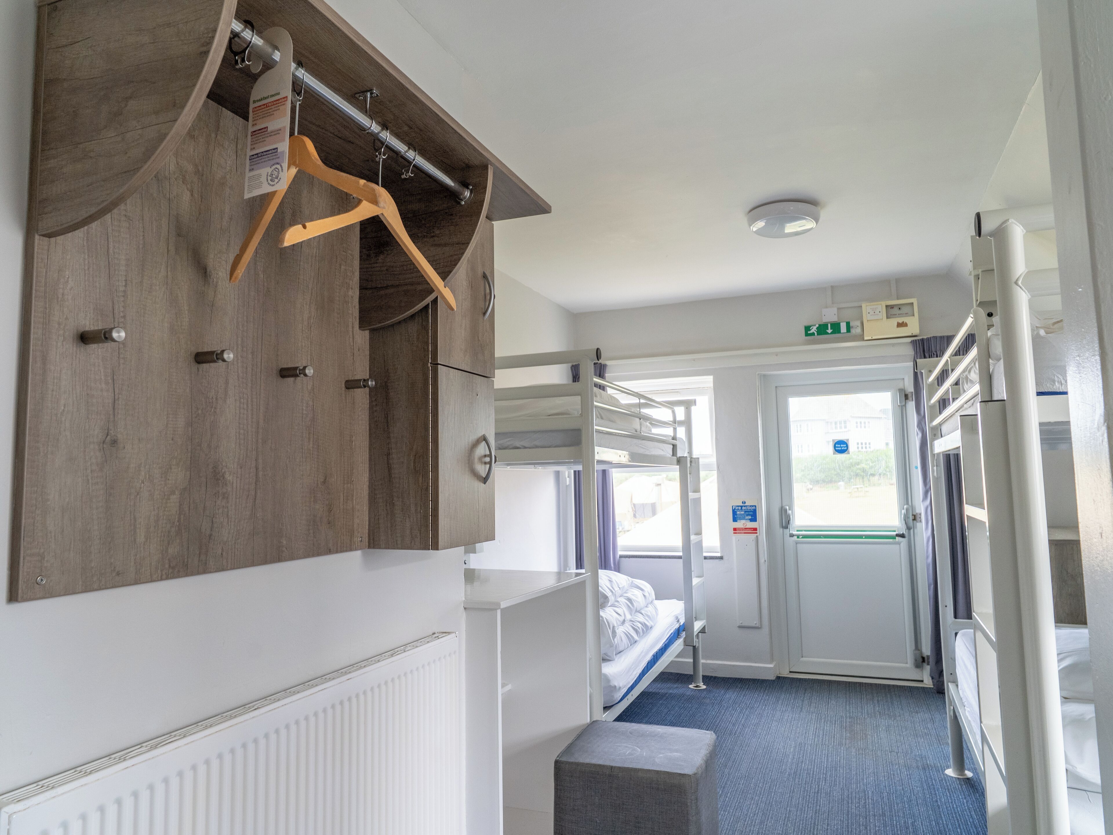 Una habitación de hotel con literas, un armario de madera, un radiador y una puerta que da al exterior.