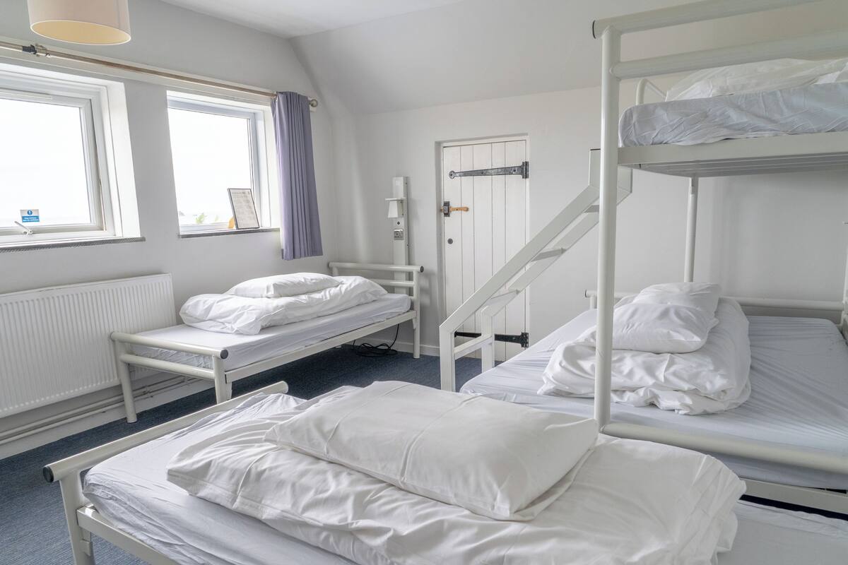 A room with bunk beds, a window with curtains, a radiator, and a door with a handle.