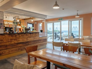 A restaurant with a wooden counter, tables, and chairs, and a view of the ocean through large windows. - YHA Treyarnon - Hostel (Padstow)