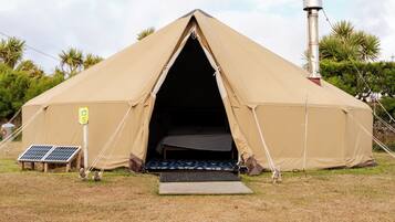 Een grote, beige tent met een deur en een kleine hellingbaan die erheen leidt. Er ligt een zonnepaneel en een metalen schoorsteen op de grond.