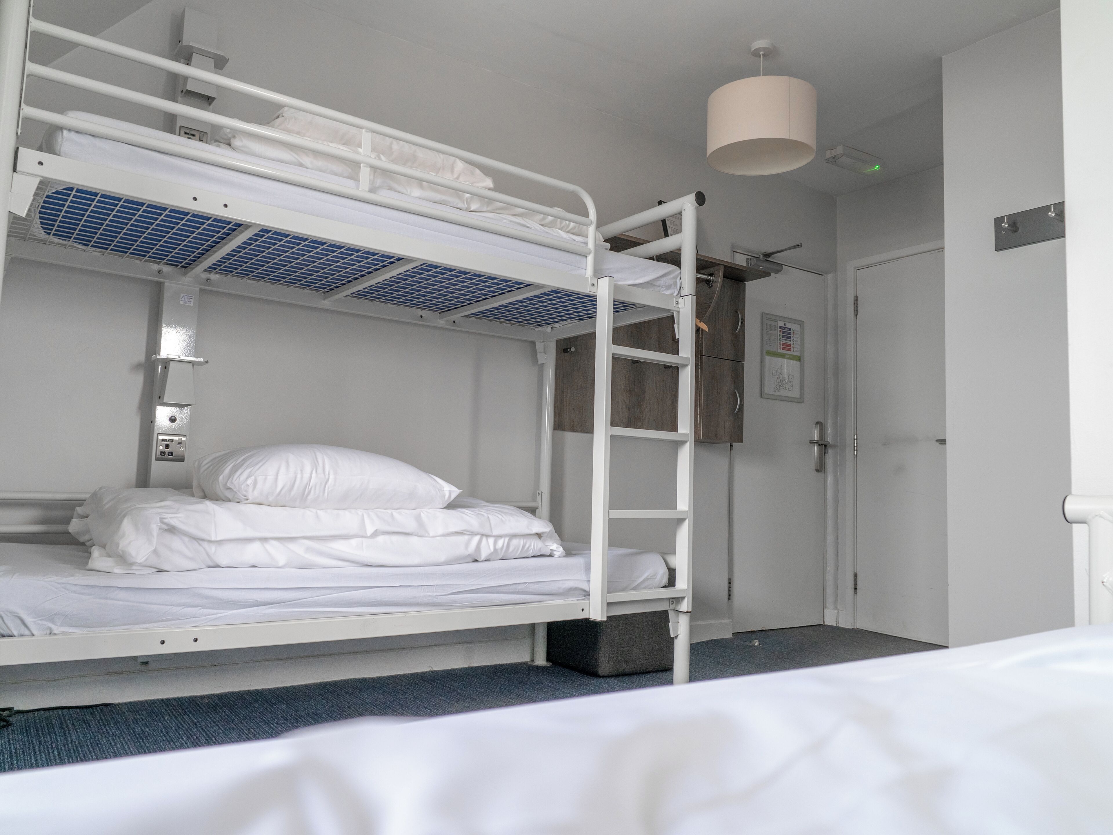 Ein Schlafraum mit Etagenbetten, Deckenventilator, Tür und Leuchte.