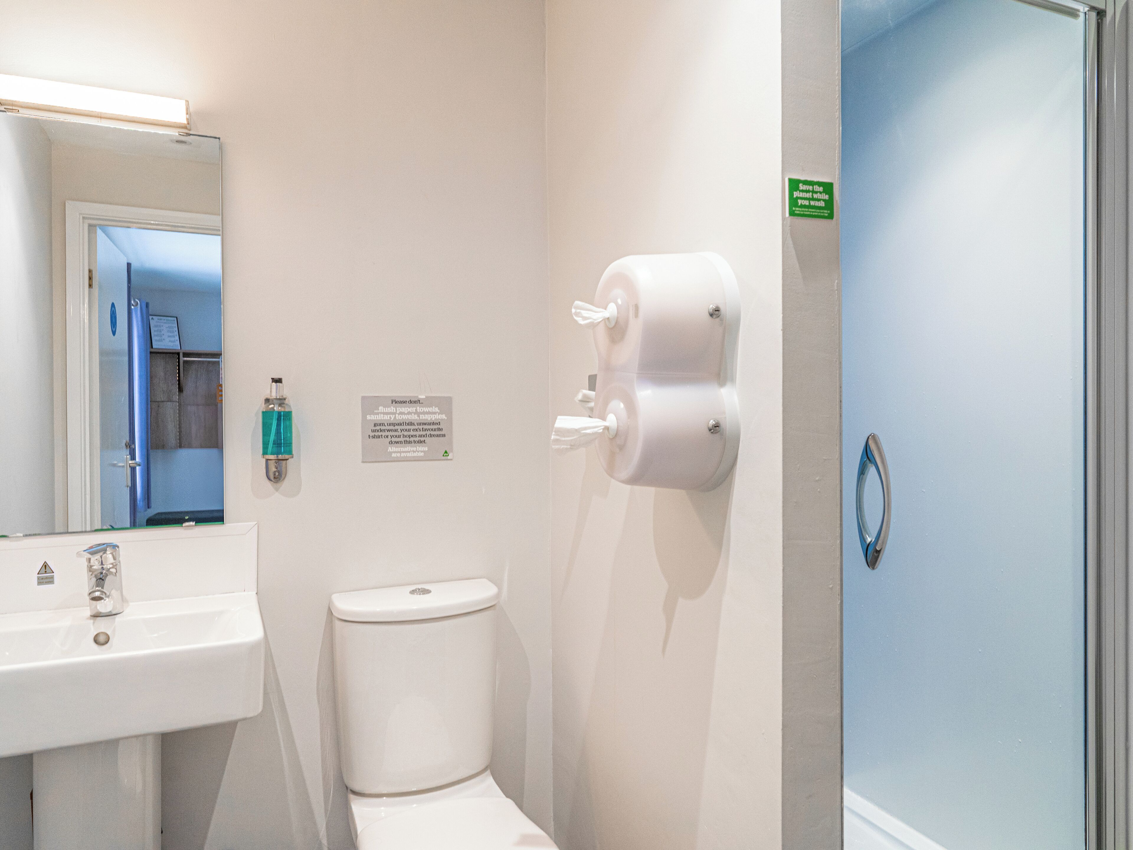 A bathroom with a sink, toilet, and hand dryer. There is a sign on the wall and a door with a sign above it.