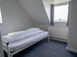Una cama individual en una habitación con techo inclinado y una ventana con cortinas.