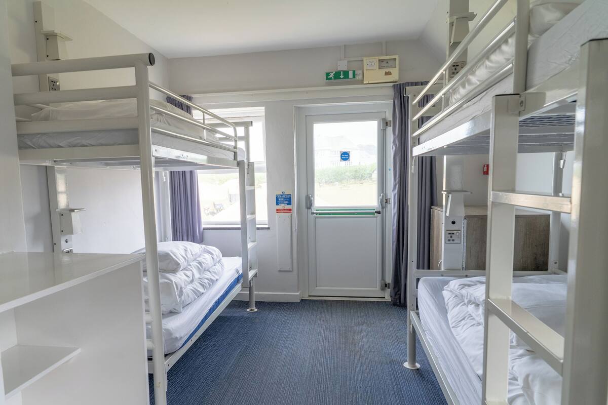 A compact hotel room with bunk beds, a small desk, and a window with curtains.