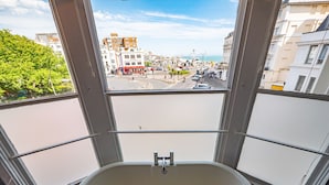 A corner bathroom with a bathtub, large windows, and a view of a cityscape. - a&o Brighton Beach (Brighton)