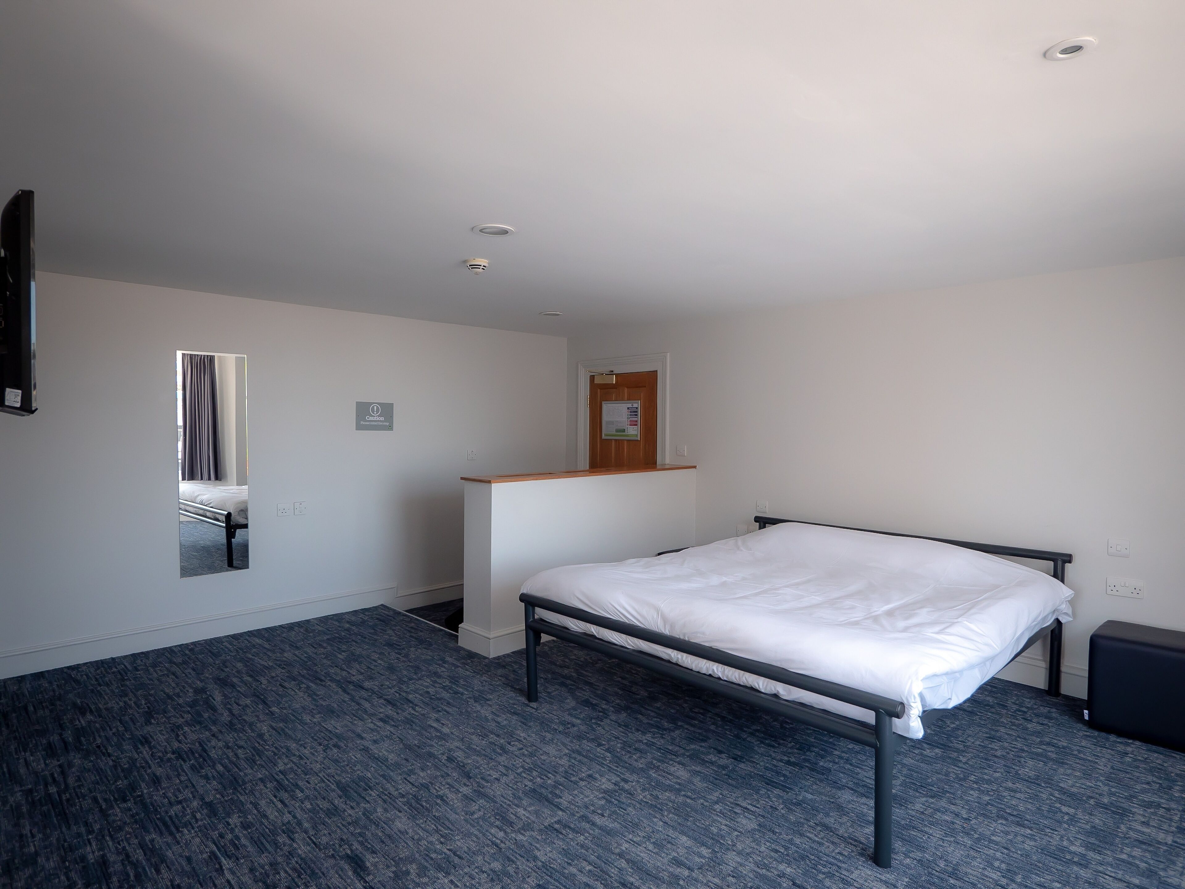 Una habitación de hotel con una cama individual, un escritorio pequeño, un espejo y una ventana con cortinas.