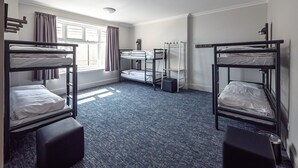 A dormitory room with bunk beds, a window with curtains, a radiator, and a ceiling light. - a&o Brighton Beach (Brighton)
