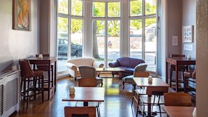 A dining area with multiple tables and chairs, large windows with a view of the street, and a chandelier. - a&o Brighton Beach (Brighton)