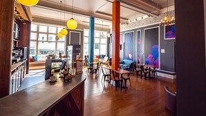 A modern cafe with wooden floors, a bar area, and colorful wall art. - a&o Brighton Beach (Brighton)