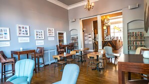 A library with wooden tables and chairs, bookshelves, and framed pictures on the walls. - a&o Brighton Beach (Brighton)