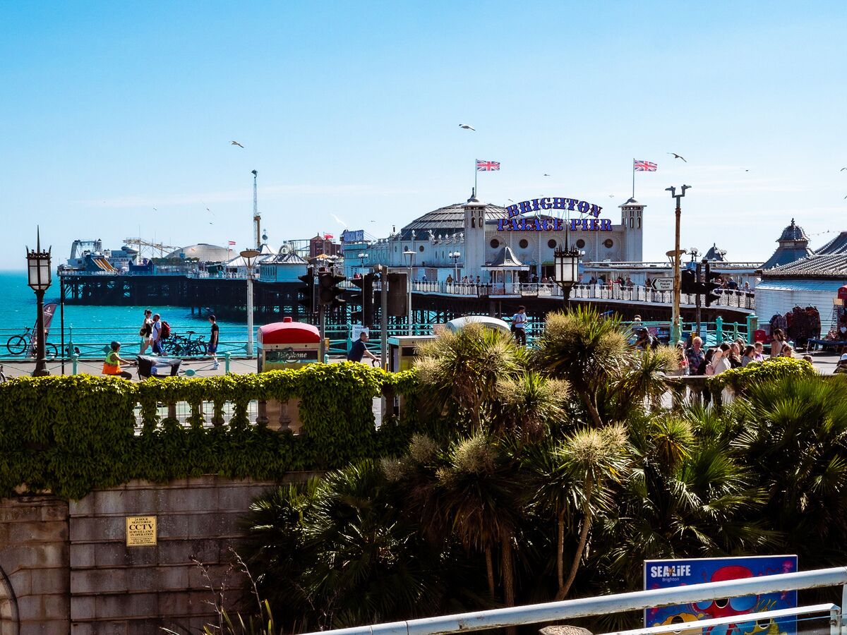 A waterfront promenade with a prominent building labeled "Brighton Palace Pier," featuring a classic architectural style with a dome and flags.