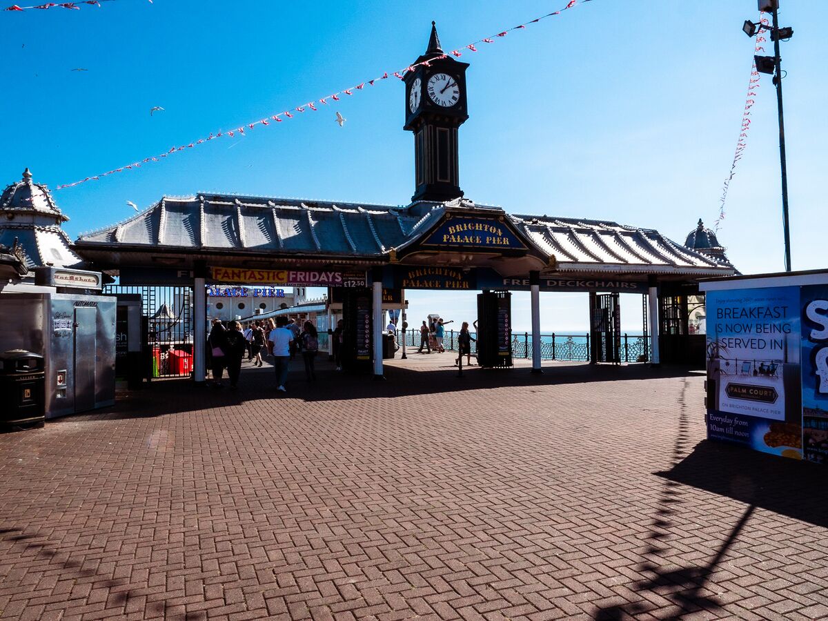A seaside promenade with a clock tower, a covered seating area, and a sign advertising breakfast.