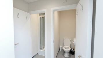 A bathroom with a toilet, a trash bin, and a shower area.