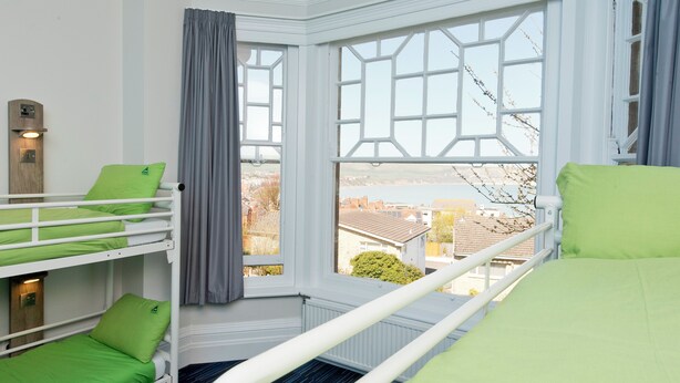 Quarto com beliches, janela com vista para edifícios e radiador.