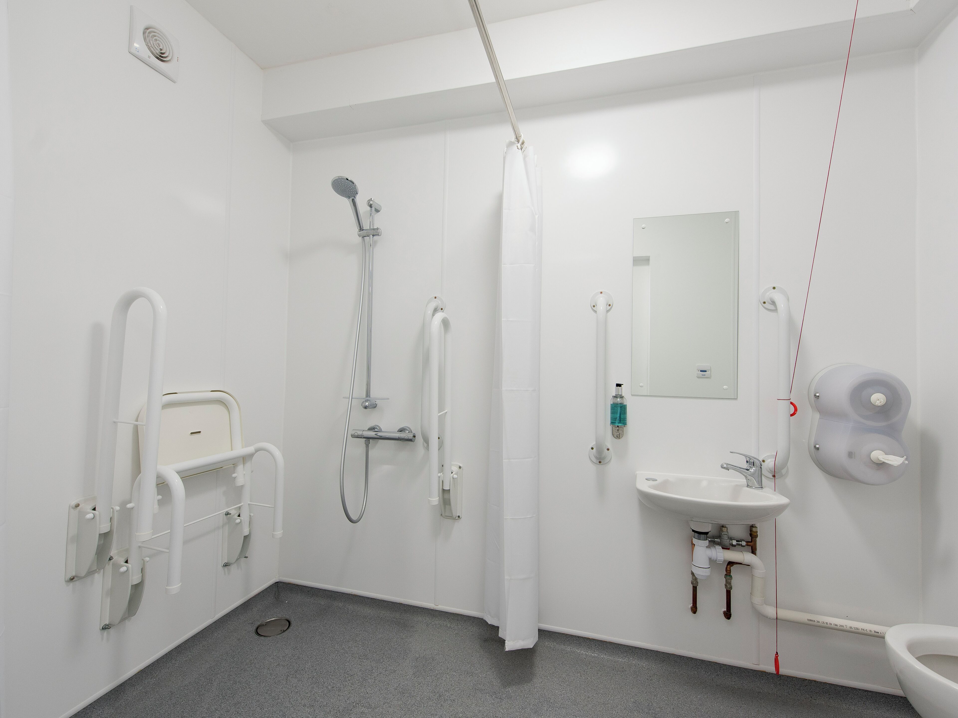 Ein modernes Badezimmer mit Bodendusche, Handlauf, Waschbecken und Toilette.