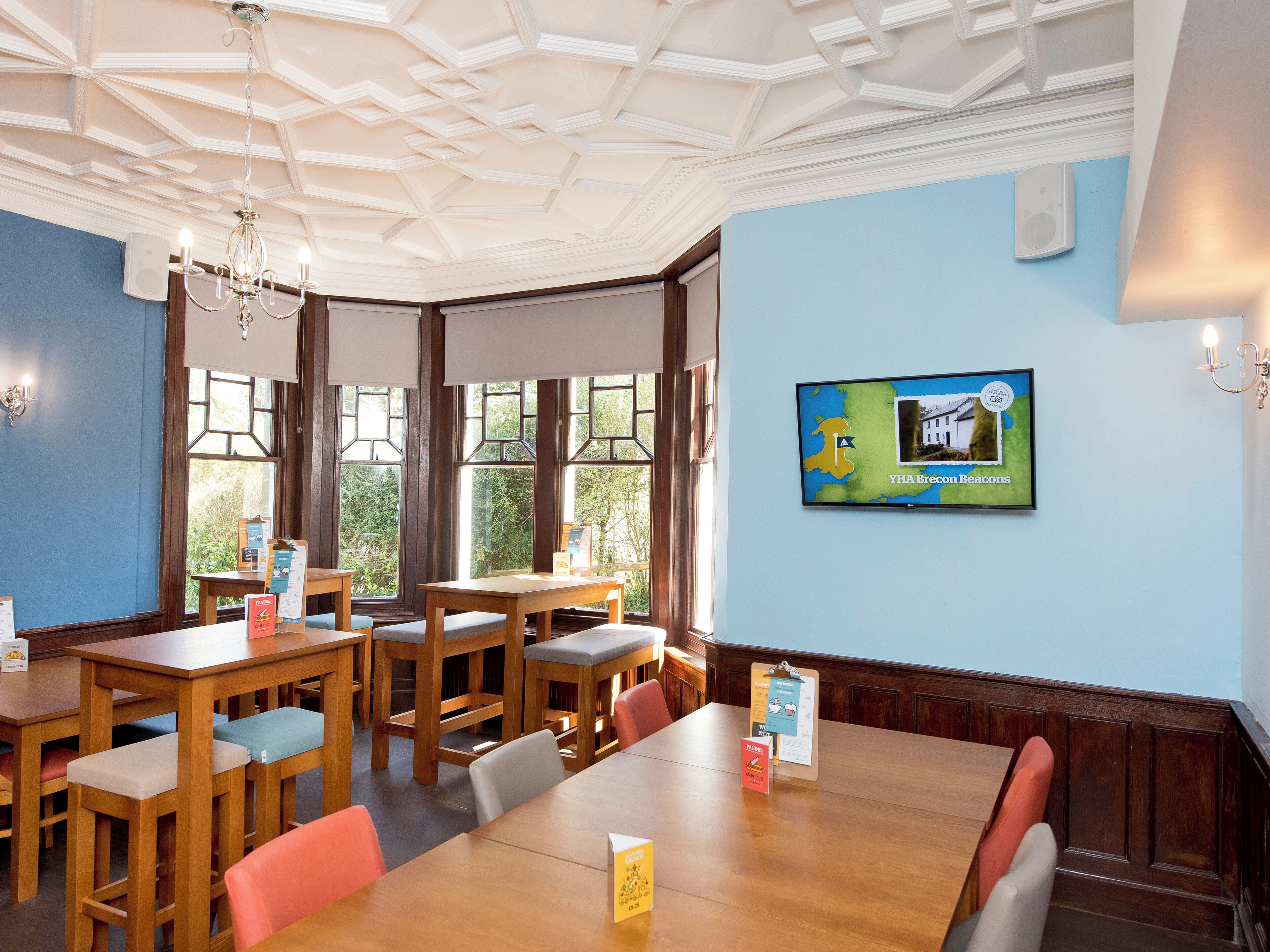 A conference room with wooden tables and chairs, a large screen displaying a map, and a ceiling with a geometric pattern.