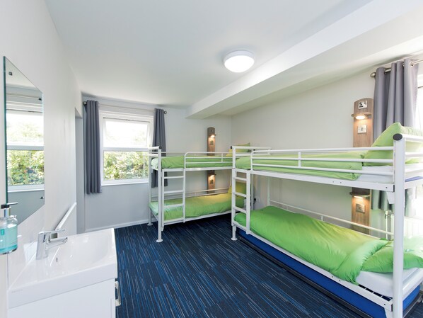 Un dormitorio con literas, tres literas, un lavamanos y un espejo.