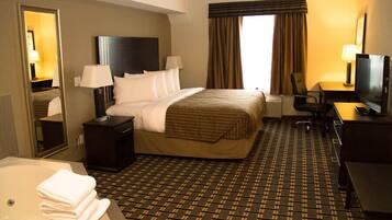 Habitación de hotel con cama, escritorio, televisión, silla, espejo y baño con bañera y toallas.