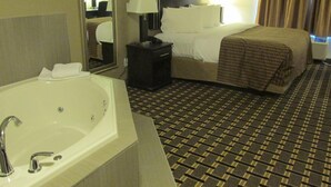 Habitación de hotel con una bañera grande, una cama con manta a cuadros, una mesita de noche con lámpara y un espejo.