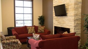 Una sala de estar con un sofá rojo, un sillón estampado, un televisor de pantalla plana montado en una pared de piedra y una chimenea.