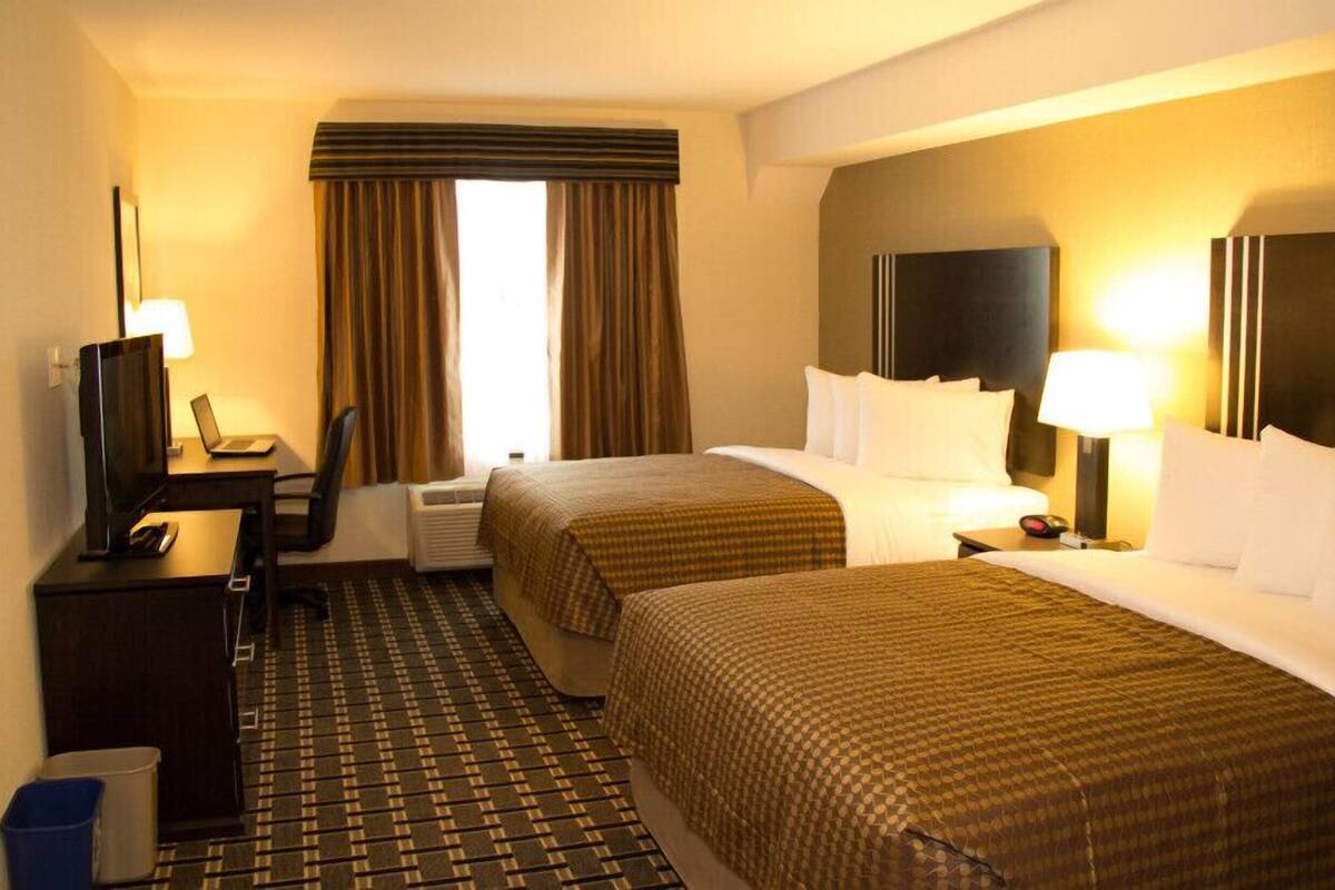 Een hotelkamer met twee bedden, een bureau met een computer, een televisie en een raam met gordijnen.